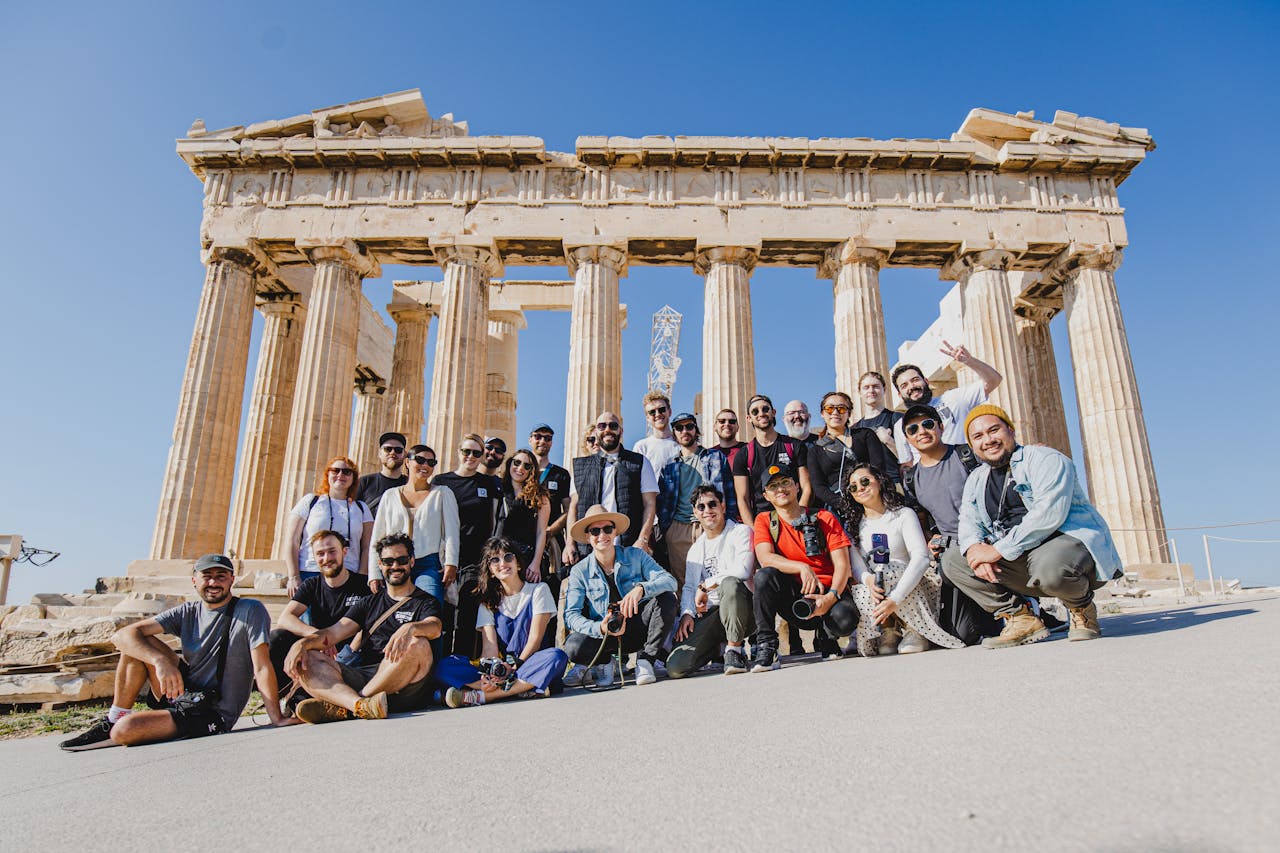 A group photo of tourists in front of the Parthenon, Athens, Greece under a clear blue sky.